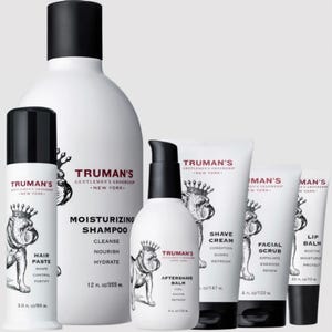 Six grooming products for men, including moisturizing shampoo, hair paste, shave cream, aftershave balm, facial scrub, and lip balm, all branded with Truman's logo.
