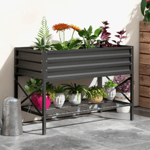 Metal raised garden bed with colorful plants above; lower shelf holds small potted plants and a watering can sits beside it on a patio.