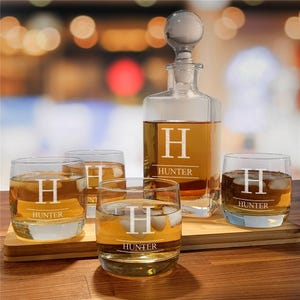 A whiskey decanter set includes a glass decanter and four glasses, each etched with a large \“H\“ and the name \“Hunter.\“