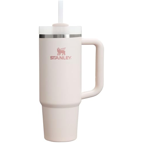 A tall, light pink insulated tumbler with a handle, featuring the \“Stanley\“ logo and a straw.