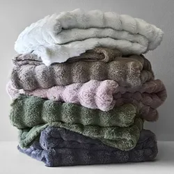 A stack of soft, fluffy blankets in various colors, including white, gray, pink, green, and dark blue, with a plush, textured design.