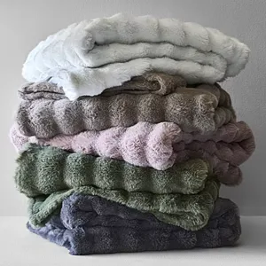 A stack of soft, fluffy blankets in various colors, including white, gray, pink, green, and dark blue, with a plush, textured design.
