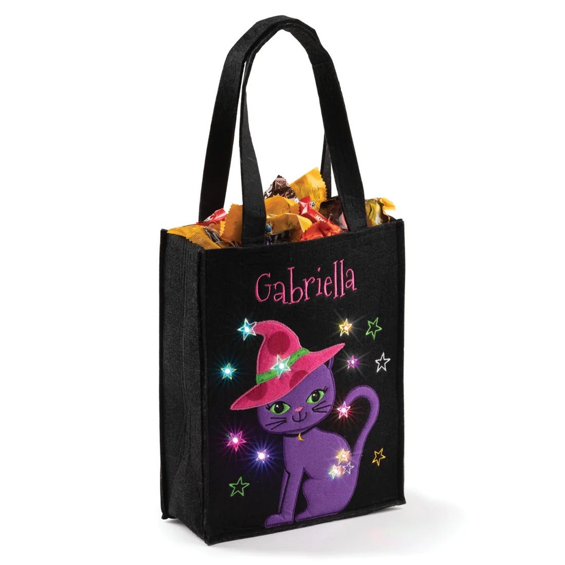 Black tote bag featuring a purple cat wearing a witch hat with stars and personalized with \“Gabriella,\“ filled with assorted candy.