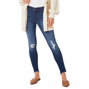 A person is wearing ripped blue skinny jeans paired with a cream cardigan and brown loafers.