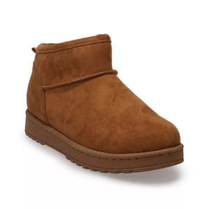 A brown suede ankle boot featuring a flat sole and minimal detailing. It has a slip-on design with a rounded toe.