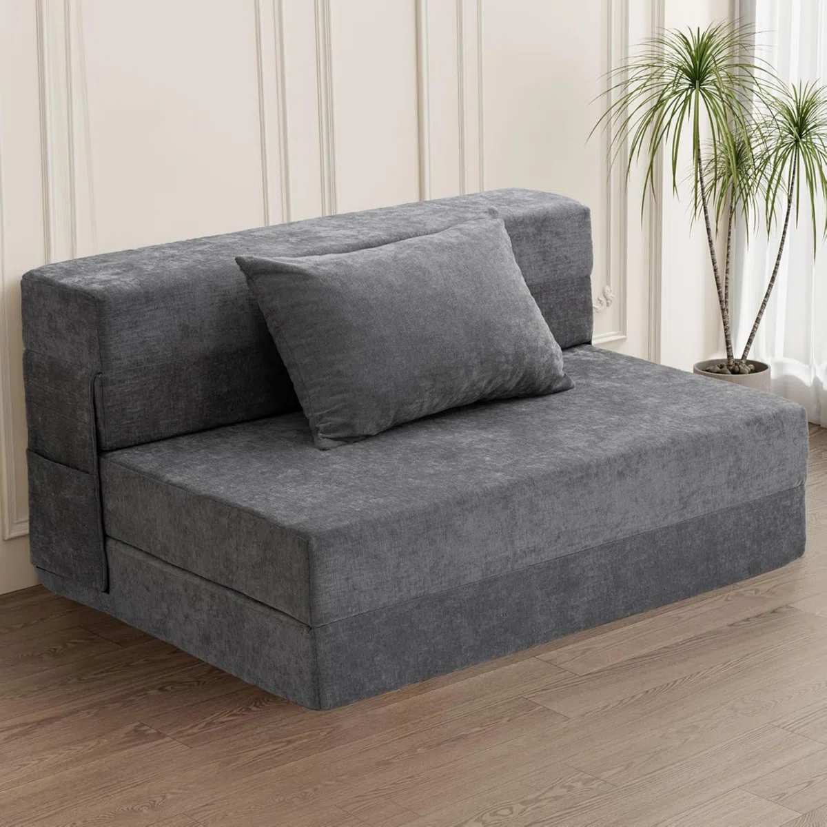 A compact, gray fabric loveseat with a cushion, featuring a minimalist design on wooden flooring, accompanied by a potted plant.