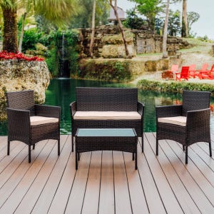 Outdoor patio set featuring a wicker loveseat, two matching armchairs with cushions, and a glass-topped coffee table, placed on a deck overlooking a pond and waterfall.