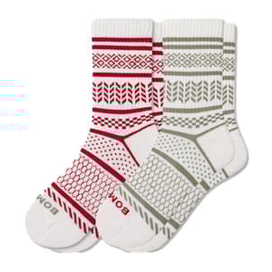 A pair of crew socks with geometric patterns, one in red and white and the other in olive and white. Each sock features brand lettering near the toe.