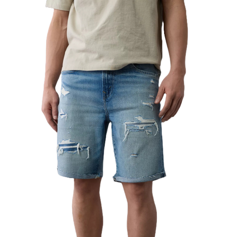 A person is wearing distressed denim shorts paired with a light beige T-shirt, featuring a casual style with various rips and frays for a relaxed summer look.