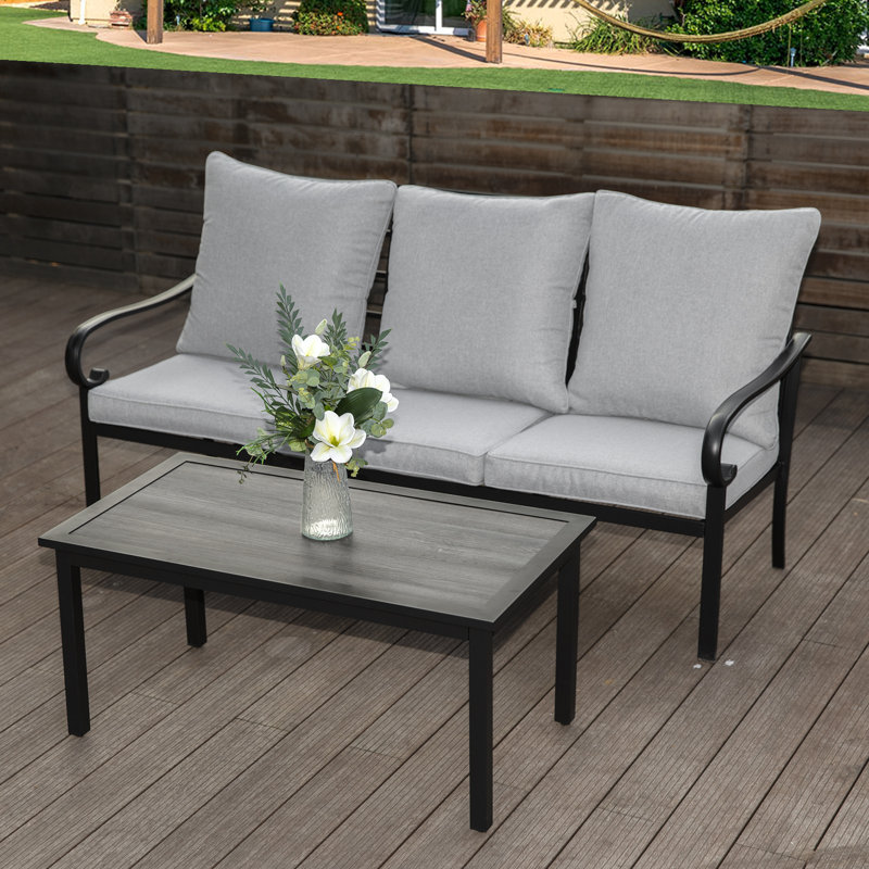 Metal-framed outdoor loveseat with gray cushions and a matching coffee table, adorned with a small vase of white flowers.