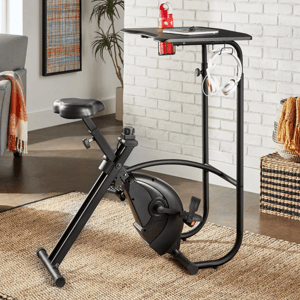 The Virgil Exercise Bike Desk features a stationary bike with an adjustable seat and pedals attached to a built-in desk with space for items, a red water bottle, and headphones. It combines a workout bike and workstation in a space-efficient design.