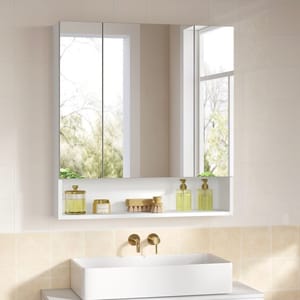 Wall-mounted bathroom mirror with hidden storage, featuring two mirrored doors and an open shelf below. White frame with dual gold dispensers and a small brush placed on the shelf.