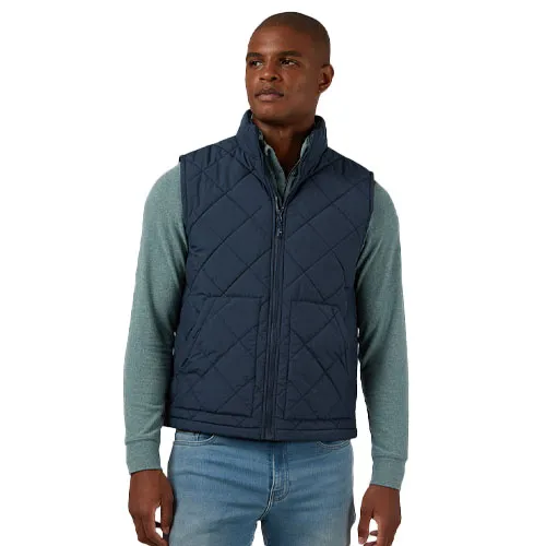 A man wears a quilted navy vest over a green long-sleeve shirt, paired with light blue jeans.