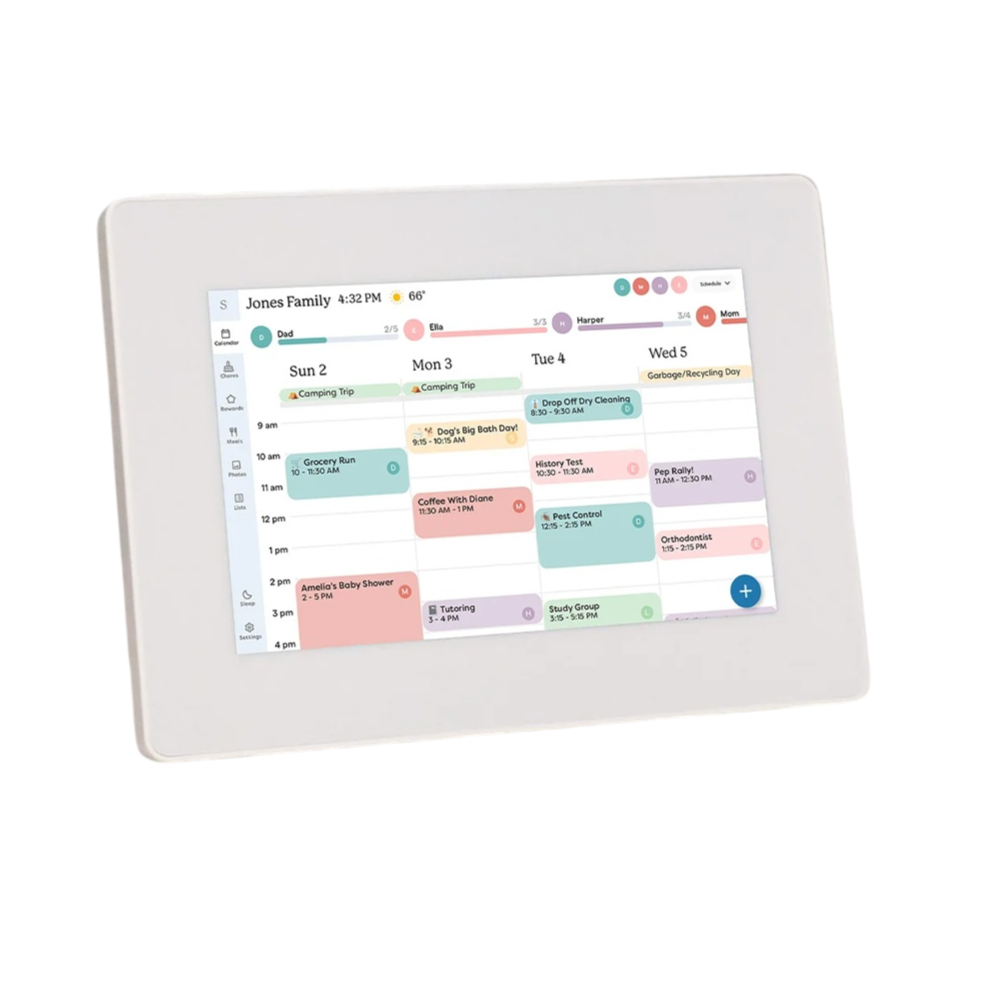 A digital calendar display stands on a kitchen counter, showing a family's weekly schedule with color-coded events and tasks, like a camping trip and appointments.