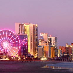Cityscape featuring a Ferris wheel illuminated at night, set against a backdrop of modern skyscrapers and a coastline.