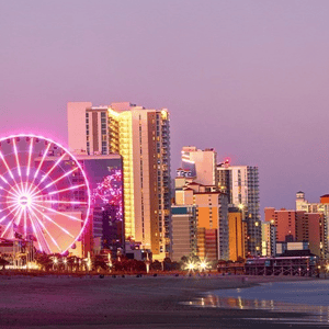 Cityscape featuring a Ferris wheel illuminated at night, set against a backdrop of modern skyscrapers and a coastline.