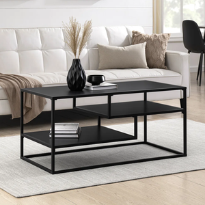Black metal coffee table with two shelves set on a light gray rug, positioned in front of a white tufted sofa. Decor includes a black vase with pampas grass, a book, a candle, beige and knit pillows, and abstract wall art.
