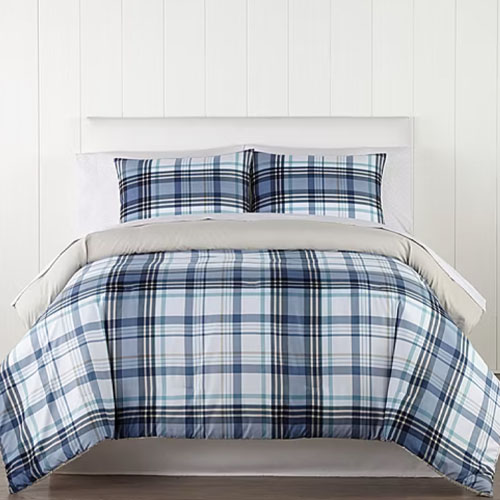 A bed features a plaid-patterned comforter and matching pillow shams in shades of blue, white, and black. The setting includes a neutral backdrop with textured white walls.