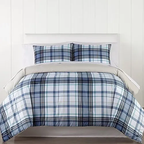 A bed features a plaid-patterned comforter and matching pillow shams in shades of blue, white, and black. The setting includes a neutral backdrop with textured white walls.