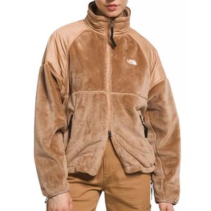 The North Face Velour Jacket is a tan, plush zip-up with a high collar and contrasting smooth fabric on the upper shoulders and arms. It features side pockets and an embroidered logo on the chest.