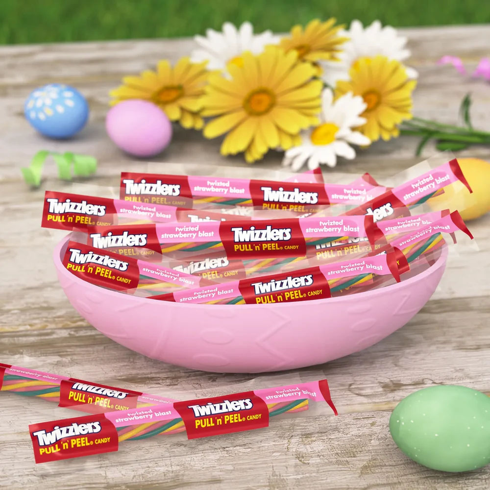 Twizzlers Pull 'n' Peel Candy, Twisted Strawberry Blast flavor, displayed in individual packages within a pink bowl, surrounded by decorative pastel-colored eggs and flowers.