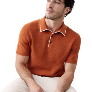 A man is wearing an orange textured short-sleeve polo shirt with a white-trimmed collar and beige pants.