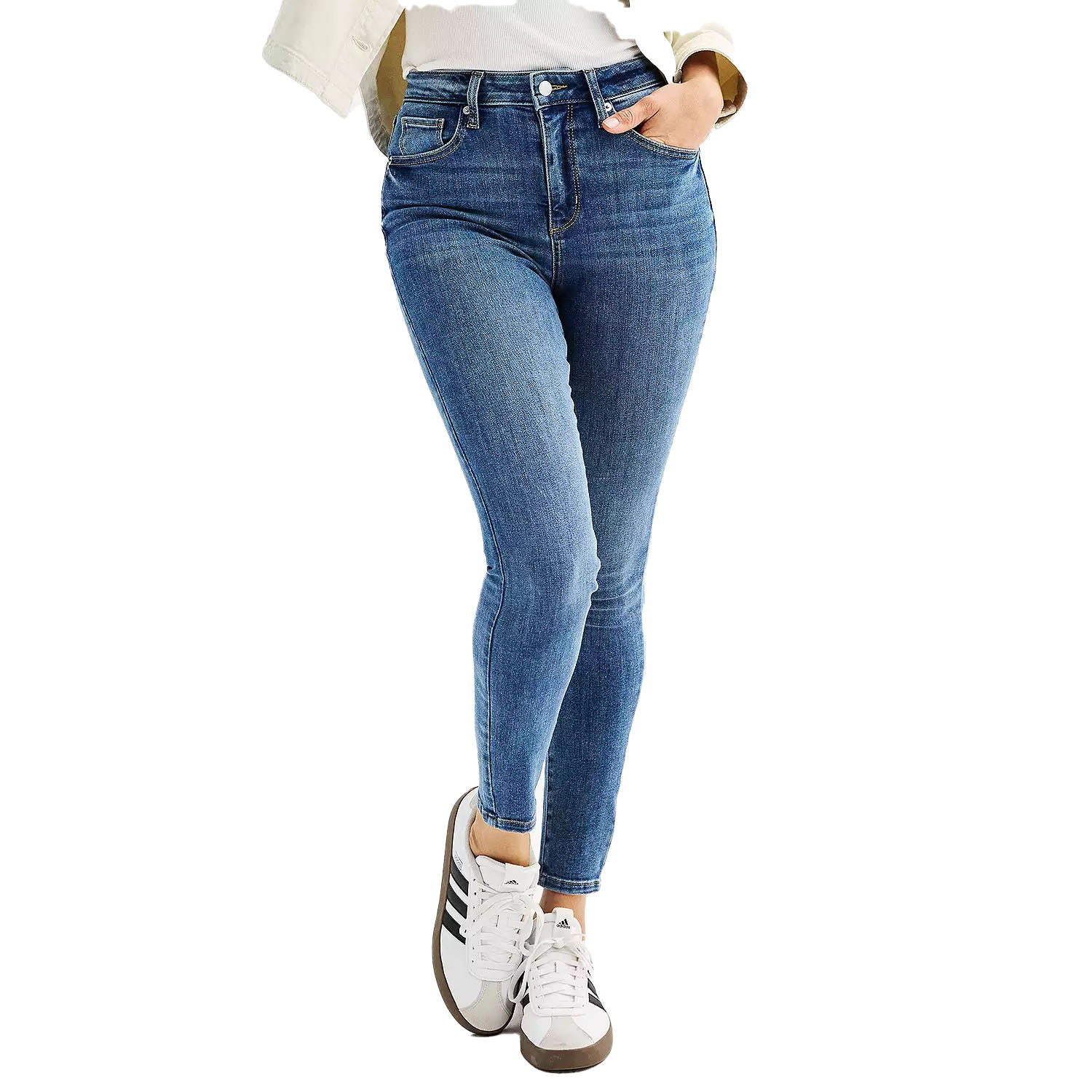 Blue high-waisted skinny jeans paired with white sneakers featuring black stripes, worn with a black belt and a white top partially covered by a beige jacket.
