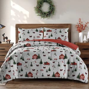 A festive bedding set featuring a winter holiday theme with snow-covered houses, red trucks, trees, and snowmen. It includes two pillowcases on a wooden bed with a wreath and holiday decorations nearby.