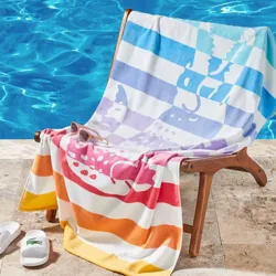 A chair by a pool is draped with a colorful striped towel featuring animal silhouettes. Nearby are white slides with a green logo and a pair of sunglasses.