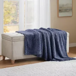 A fluffy blue throw blanket draped over a light-colored cushioned storage bench by a window with sheer curtains, next to a minimalist painting.