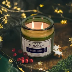 M. Baker candle labeled \“Balsam + Berries\“ is lit, surrounded by decorative lights, red berries, and star-shaped cookies.