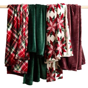 Four hanging blankets with various patterns and textures, featuring plaid, green ribbed, and red star designs.