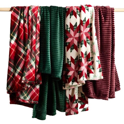 Four hanging blankets with various patterns and textures, featuring plaid, green ribbed, and red star designs.