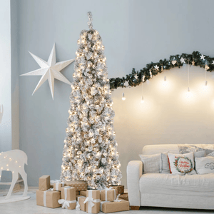 A tall, flocked Christmas tree with warm lights is surrounded by wrapped gifts. The room features a white star decoration, a garland with hanging lights, a white reindeer figure, and a beige couch with festive pillows.