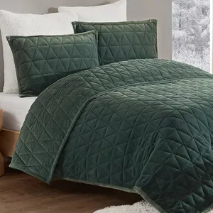 A plush, diamond-quilted green comforter with matching pillow shams is displayed on a bed, accompanied by white pillows in a cozy room setting.