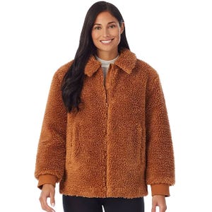 A woman is wearing a brown sherpa bomber jacket with a plush, textured surface, collar, and front zipper. It has long sleeves, two pockets, and ribbed cuffs.