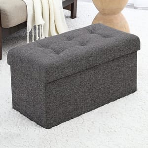 Gray upholstered storage ottoman with tufted top, placed on a white carpet.