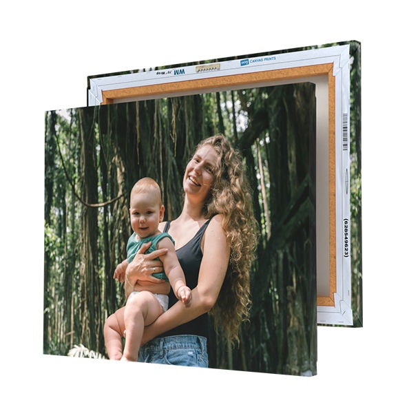 A printed canvas featuring a woman holding a baby in a forest is displayed with its wooden frame partially visible at the back.