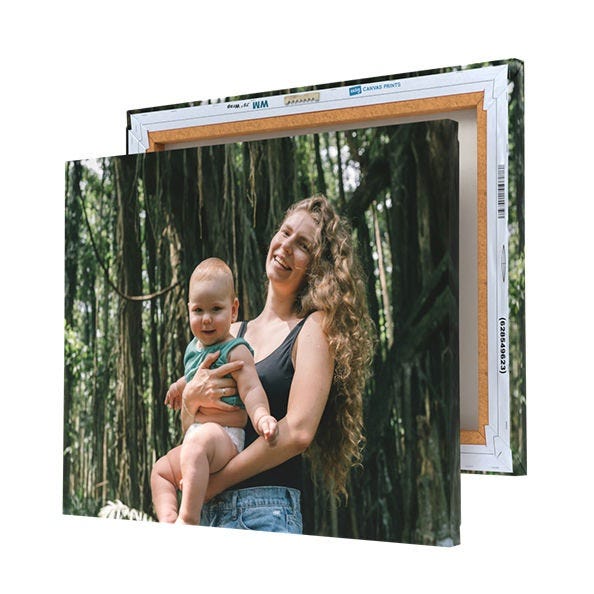 A printed canvas featuring a woman holding a baby in a forest is displayed with its wooden frame partially visible at the back.
