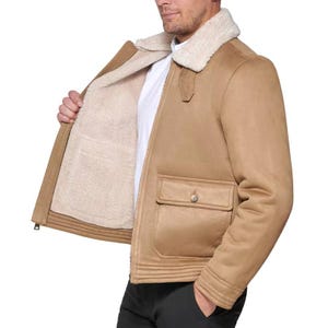 A tan faux suede jacket with shearling lining, featuring a classic design with a buttoned front pocket and a shearling collar, worn over a white shirt.