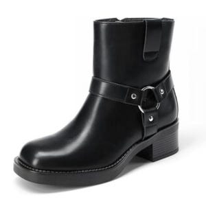 A black ankle boot with a low heel, featuring a decorative strap and metal ring detail.