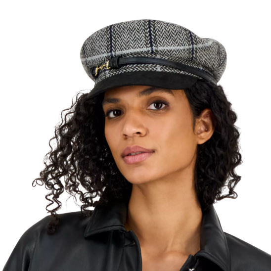 A person is wearing a black faux leather shirt jacket with two chest pockets and silver buttons, paired with a gray herringbone-patterned captain's cap featuring a black leather band and gold buckle.