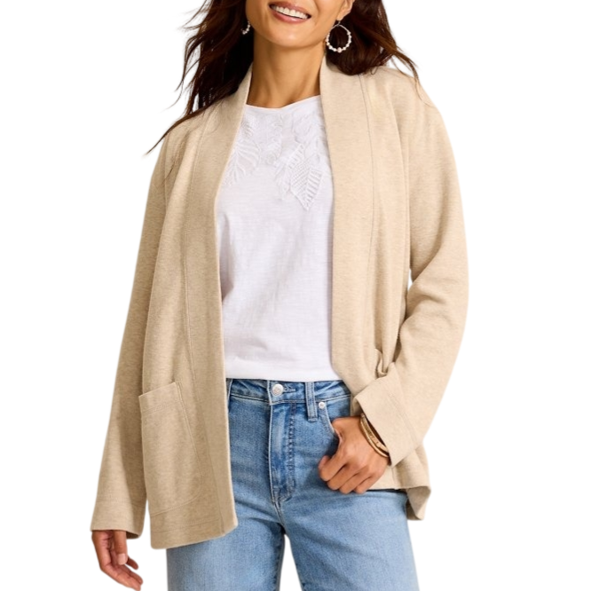 A woman is wearing a beige cardigan over a white embroidered blouse and light blue jeans, accessorized with hoop earrings and a bangle.