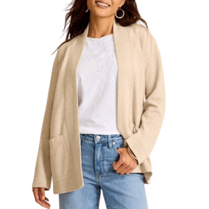 A woman is wearing a beige cardigan over a white embroidered blouse and light blue jeans, accessorized with hoop earrings and a bangle.