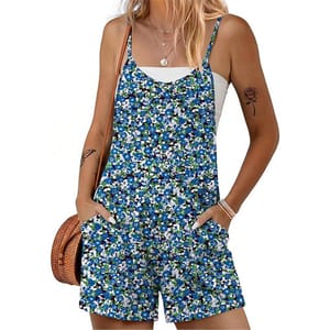 A woman is wearing a blue floral romper with spaghetti straps over a white tank top. She accessorizes with layered necklaces, bracelets, a tattoo of a rose on her arm, and holds a brown woven bag.