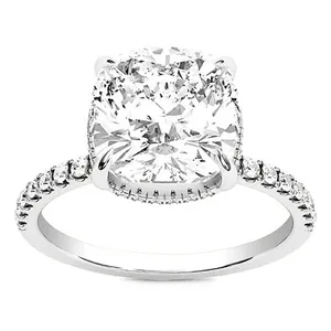 A silver-toned ring featuring a large cushion-cut diamond set in a four-prong setting, with a band adorned with smaller round diamonds.