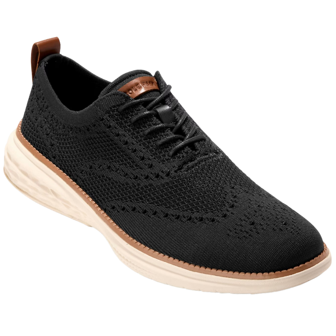 A black knit oxford sneaker with intricate stitching, a contrasting tan leather pull-tab, and a beige cushioned sole.