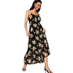 A woman is wearing a black floral maxi dress with spaghetti straps and a ruffled hem, paired with black open-toe heels.