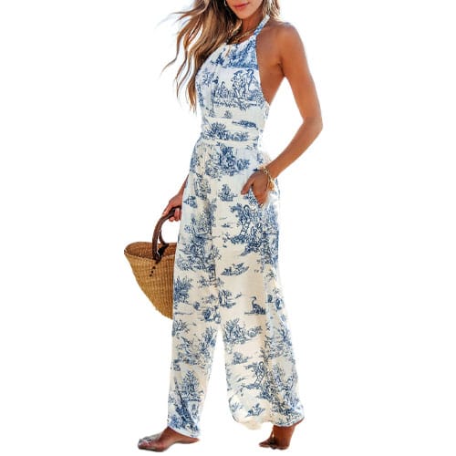 A woman wearing a sleeveless, halter-style jumpsuit with a blue and white toile pattern, holding a woven handbag.