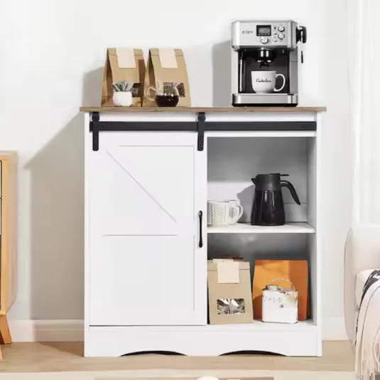 A white cabinet with a wooden top features a sliding door, revealing shelves holding coffee-related items. On top, a coffee machine is accompanied by paper bags and a potted plant.